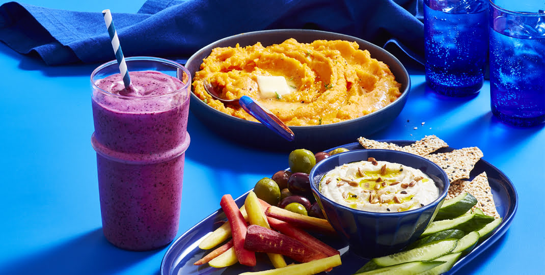 Glass with cauliflower smoothie, with sweet poato mash, and hummus in background